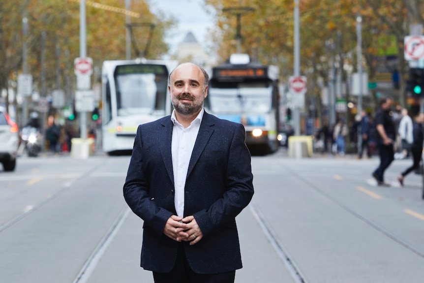 A man stands in the middle of a Melbourne street with trams in the background
