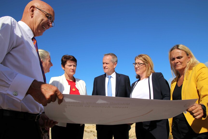 Labor Leader Bill Shorten in suit and blue tie, with several WA Labor Party people, inspect a map.