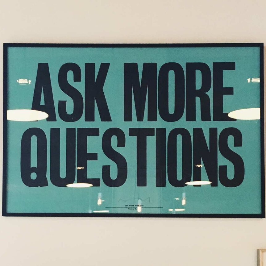 Framed poster on a shop wall which says "Ask more questions"