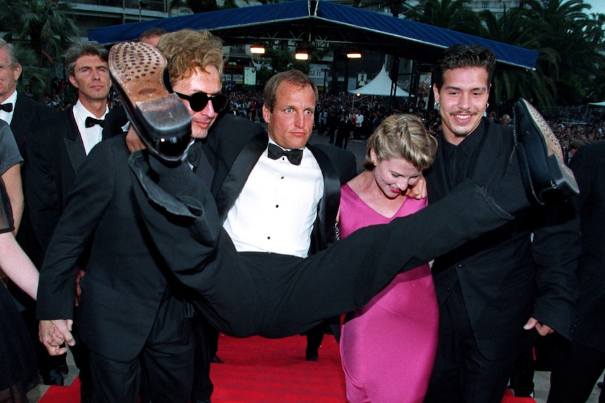 A group of people holding up a man in a suit with his legs spread out.