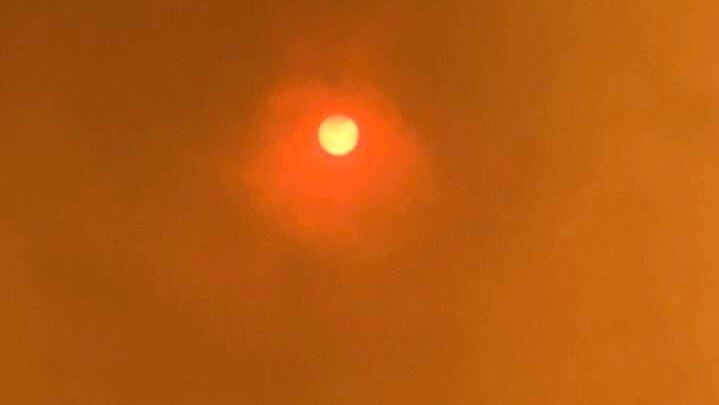 The sun shines through a sky turned yellow by smoke from a bushfire.