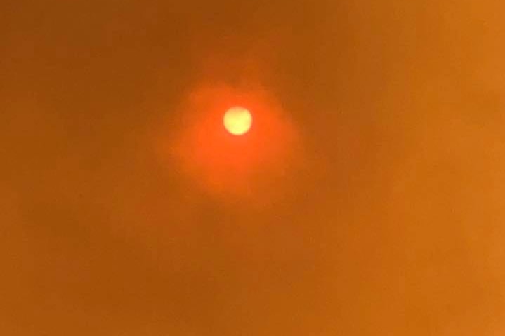 The sun shines through a sky turned yellow by smoke from a bushfire.