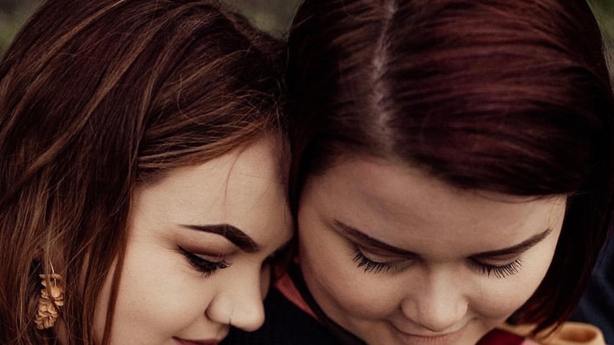 A woman with brown hair rests her head on the shoulder of another woman.