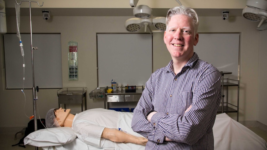 Dr Rhys Thomas stands in a simulation operating theatre.