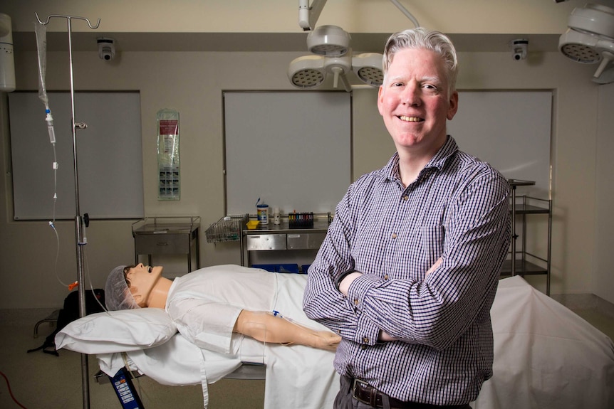 Dr Rhys Thomas stands in a simulation operating theatre.