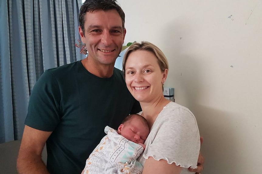 A man and woman hold their newborn baby in a hospital room.