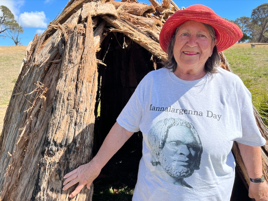 A woman in a red hat front of a bark hut 