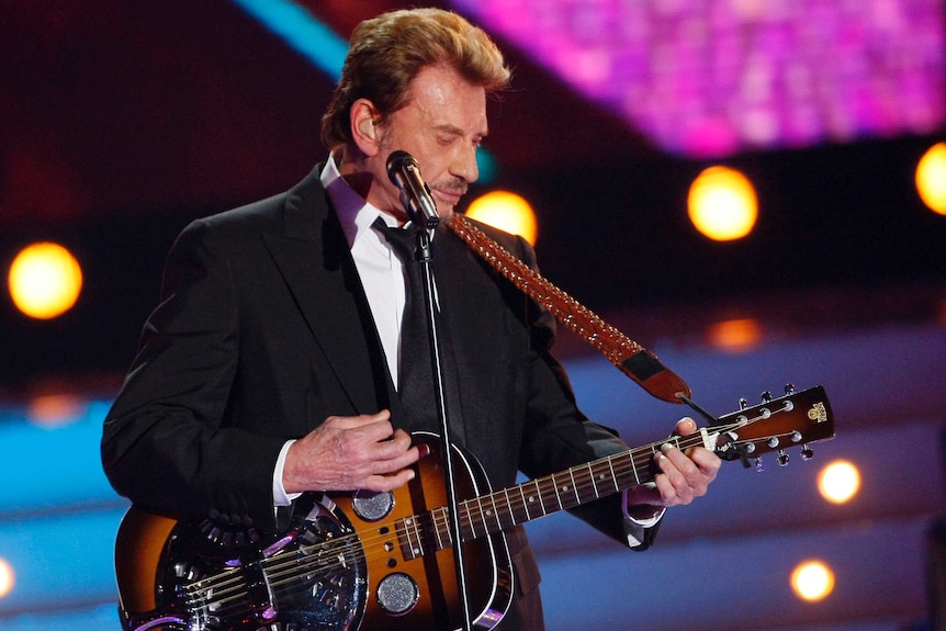 Johnny Hallyday strums his guitar in front of bright lights at the Miss France 2008 election