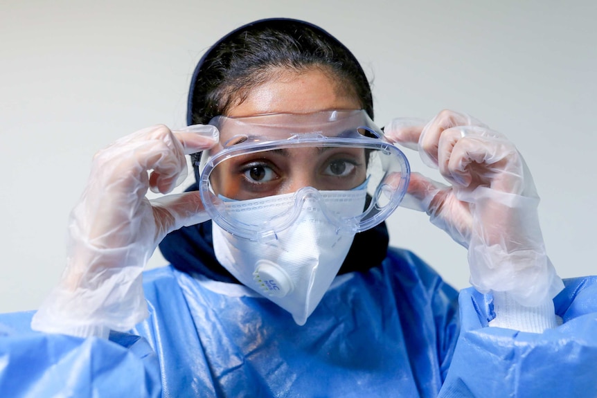 A female nurse in PPE adjusting her goggles