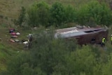 A bus on its side at the bottom of an embankment with luggage strewn around it.
