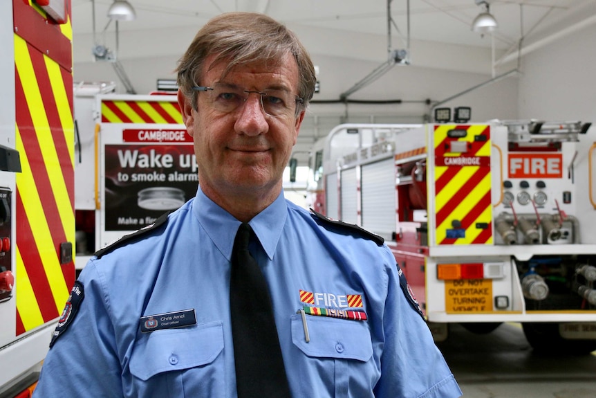 A middle-aged man in uniform stands in front of fire engines