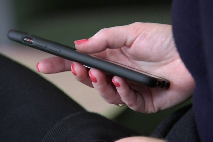 Close-up image of a womans hand with red nail polish and wedding ring on holds black phone.  