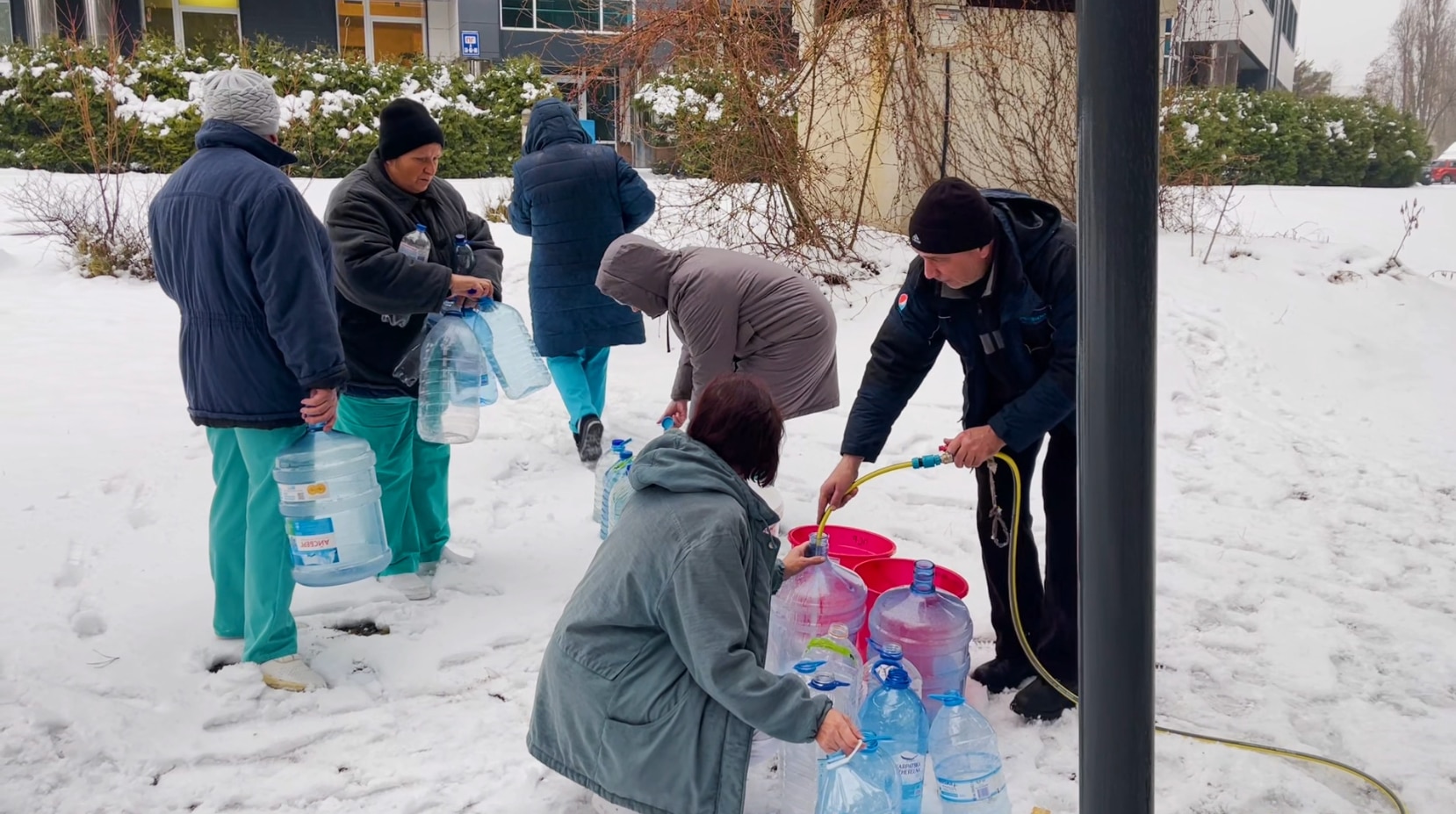 Las enfermeras afuera, en la nieve detrás del hospital, llenan barriles de agua. 