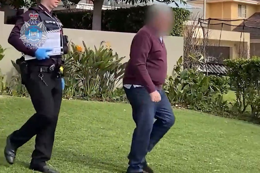 Man wearing burgundy jumper with face blurred being escorted by uniformed police officer