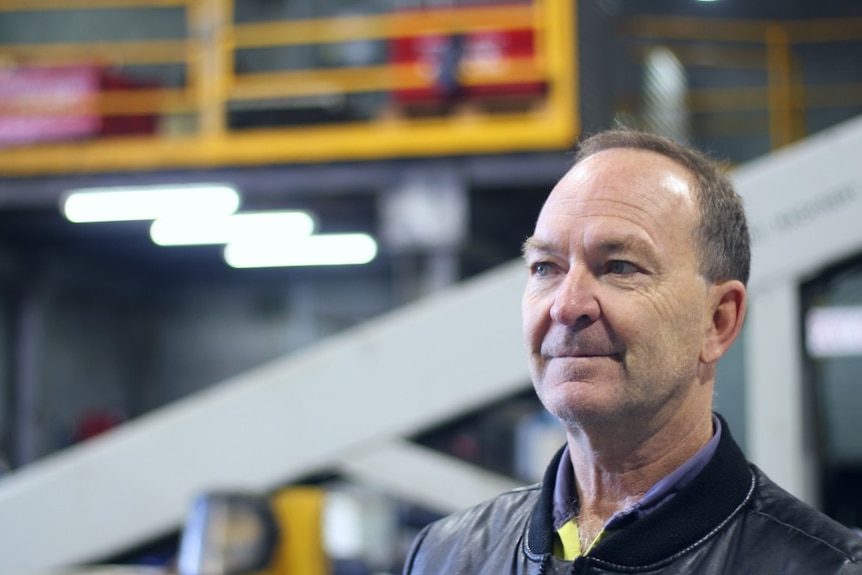 A man's face in the right of the picture, in an industrial workshop