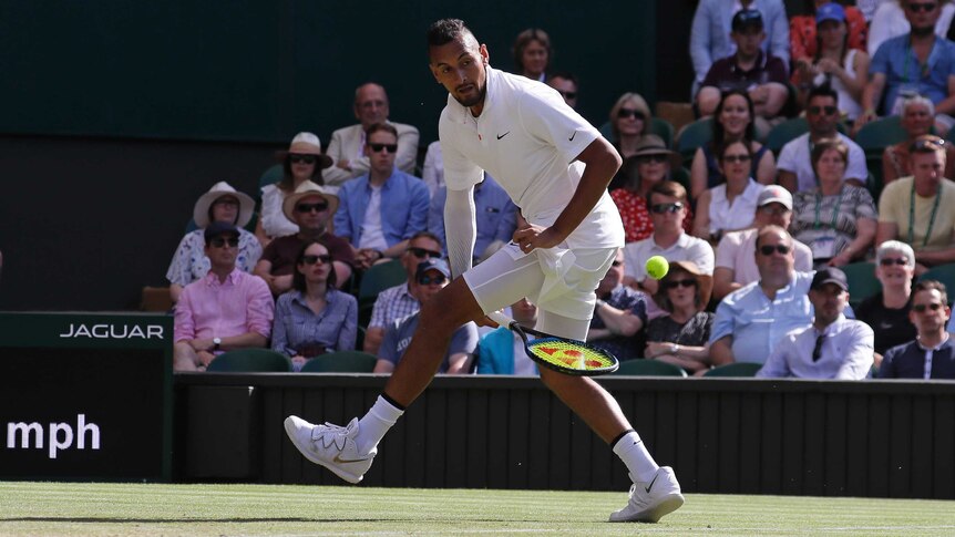 Nick Kyrgios plays a shot with his racquet between his legs