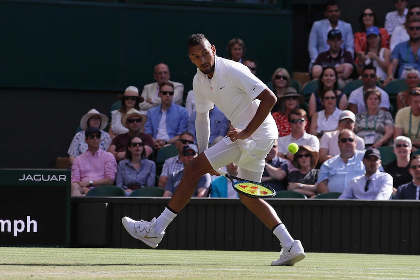 Nick Kyrgios plays a shot with his racquet between his legs