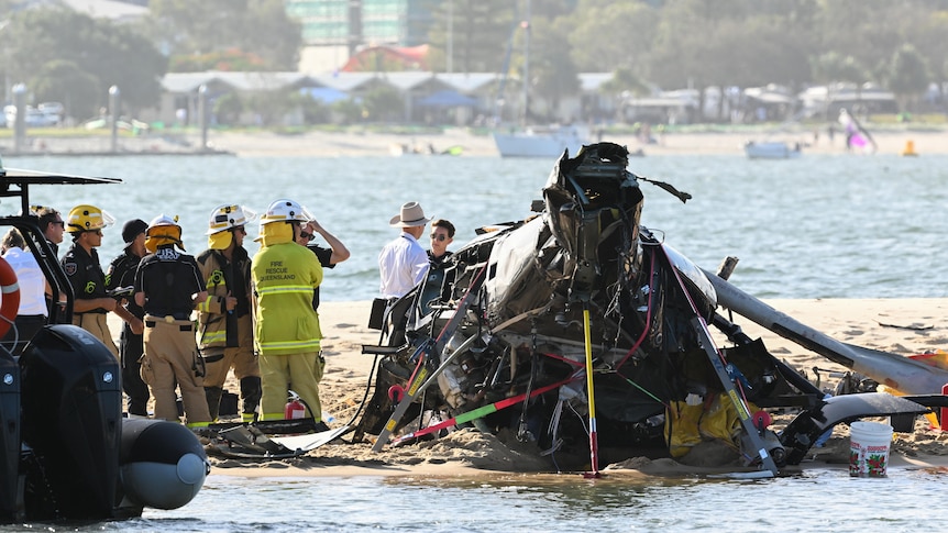Many emergency people stand near the wreckage of a helicopter