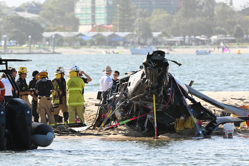 Many emergency people stand near the wreckage of a helicopter