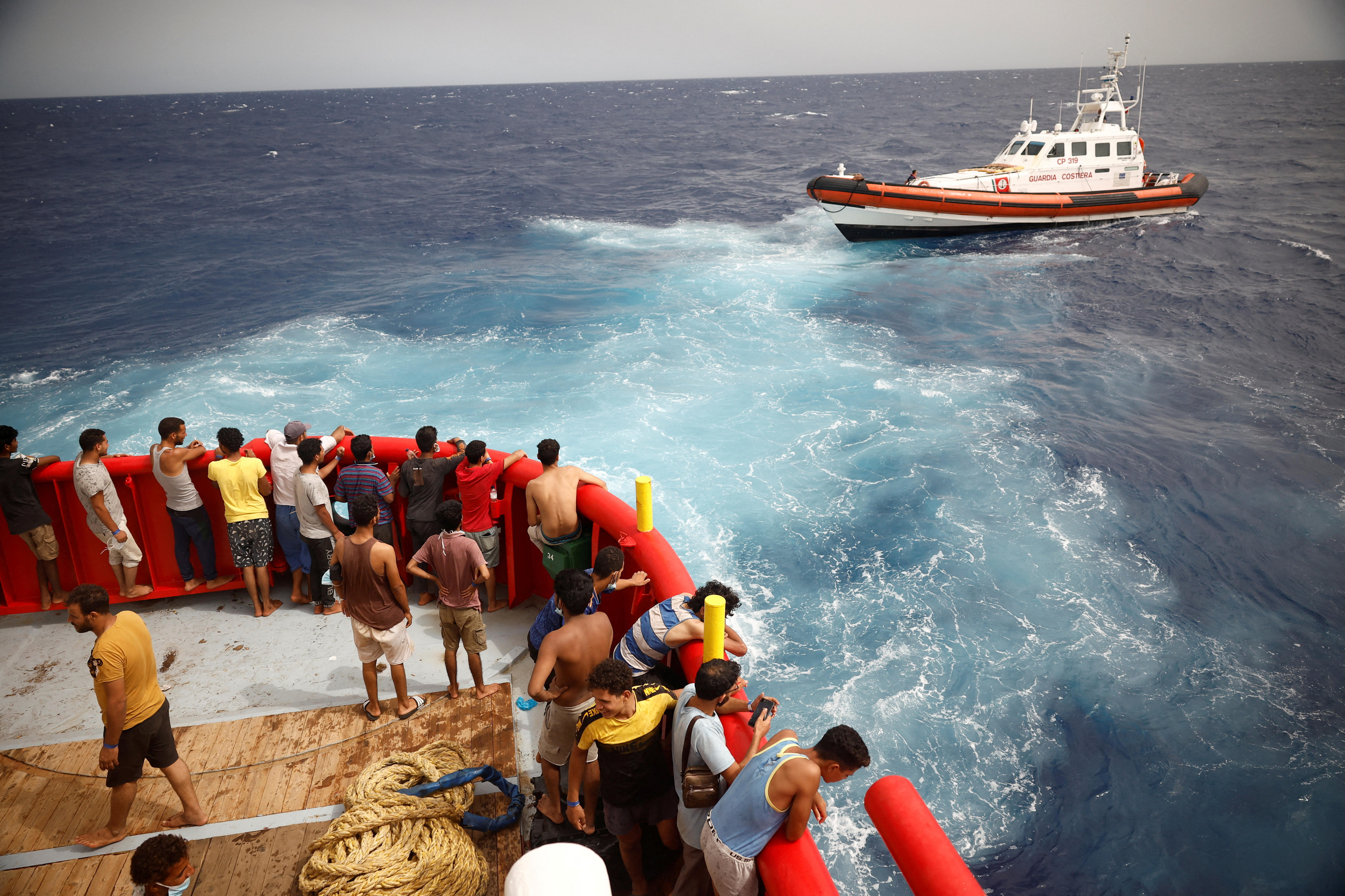 People stand around in red boat while another boat come towards them 