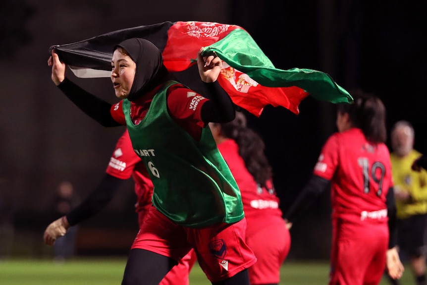 Adiba runs holding the Afghan flag above her head during a match with the Melbourne Victory Afghan Women's Team