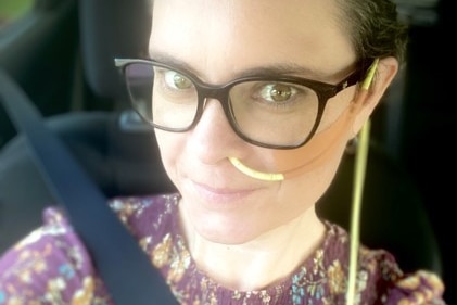 a woman sitting in a car with a seatbelt on taking a selfie with a feeding tube clearly seen on her face