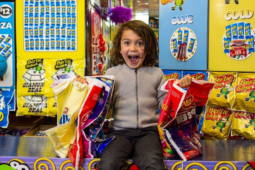 A boy holds showbags in the midst of a colourful showbag stand.