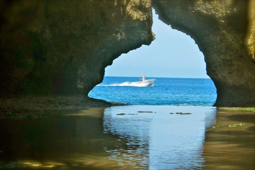 A small boat, seen through a pair of overhanging rock formations, makes its way out to sea.