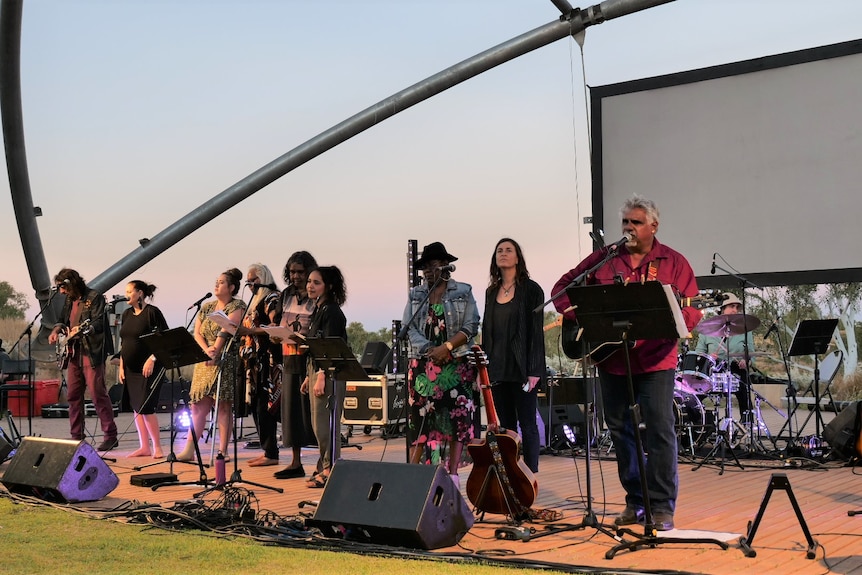 A group of singers and musicians performing at an outside stage. 