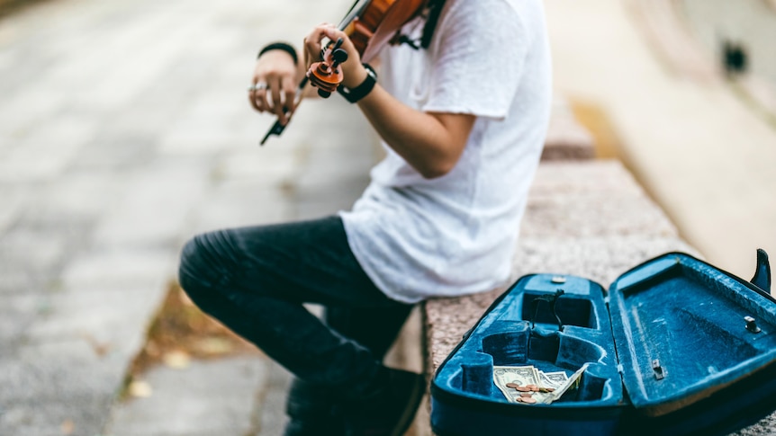 A man busks on the street, playing the violin.