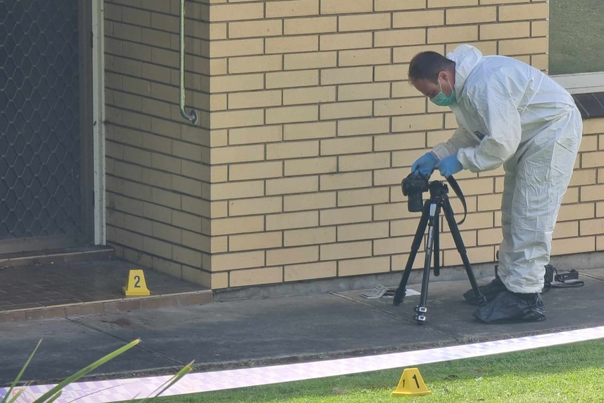 A police officer dressed in white overalls and gloves photographing a stain