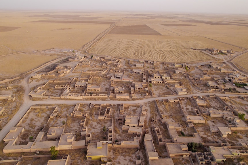 From the air, the remains of a town destroyed by war, tan-coloured buildings blending into the desert surrounds