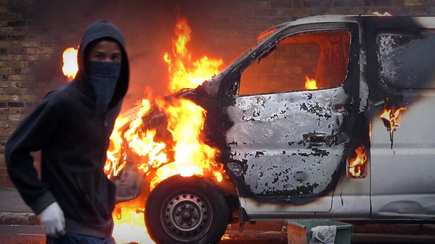 A hooded youth walks past a burning vehicle in Hackney, east London. [Getty Images: Peter Macdiarmid]