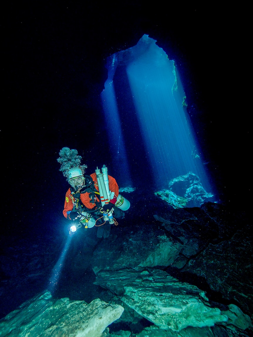 A scuba diver floats through clear water, a fluorescent blue light beam behind him.