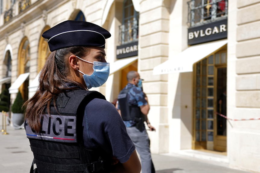 Une policière portant un gilet pare-balles et un masque facial se tient devant un magasin Bulgari. 