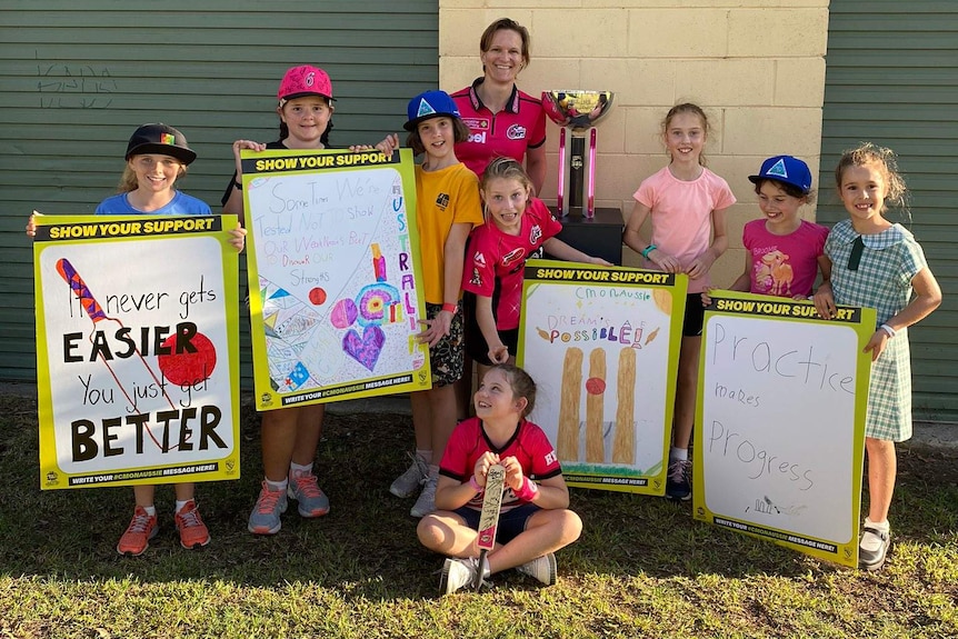 Junior female cricketers pose with the BBL trophy and a WBBL player.