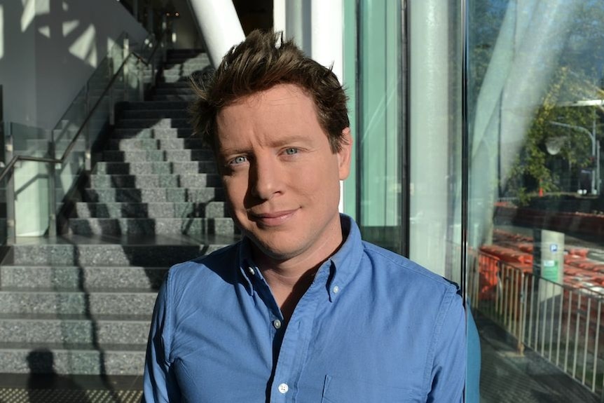 Man in collared shirt stares at camera smiling slightly