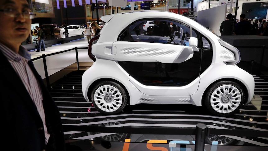 A futuristic looking small black and white vehicle sits on display stage with the text LSEV visible