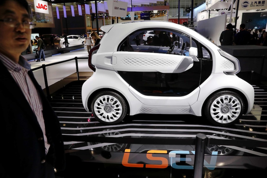 A futuristic looking small black and white vehicle sits on display stage with the text LSEV visible