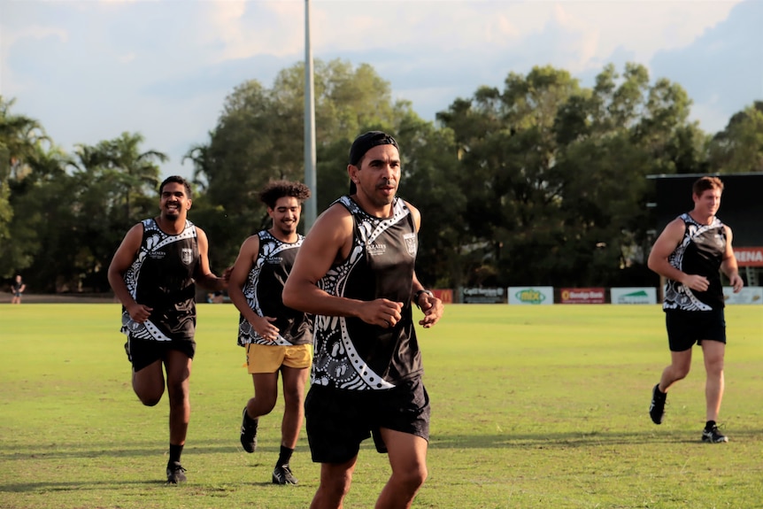 Eddie Betts runs on the Palmerston football oval with three teammates behind him.