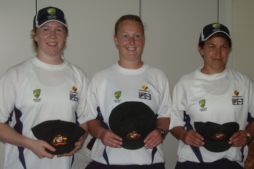 Three women are smiling, holding their Test caps.