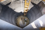 A view looking down into a concrete shaft with water and an excavator at the bottom.