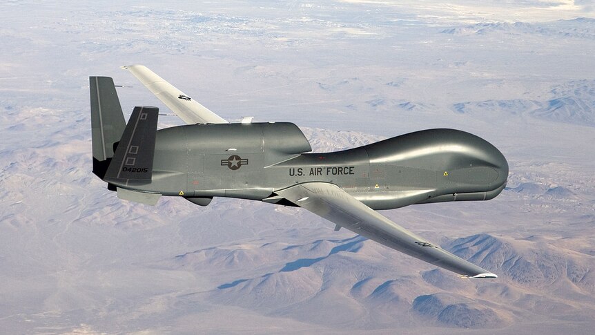 A drone marked with a US air force tag flies over barren land.