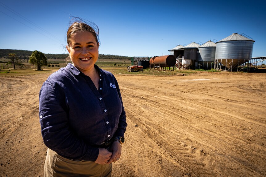 A women smiles forward, standing in front of a dirt road.