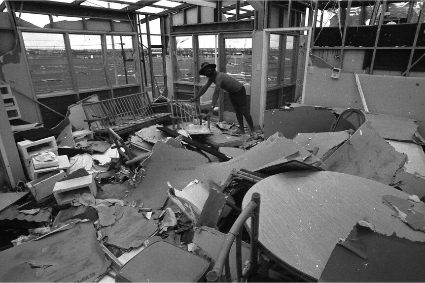 Black and white photo of building damage. Man with shirt leads on a chair.