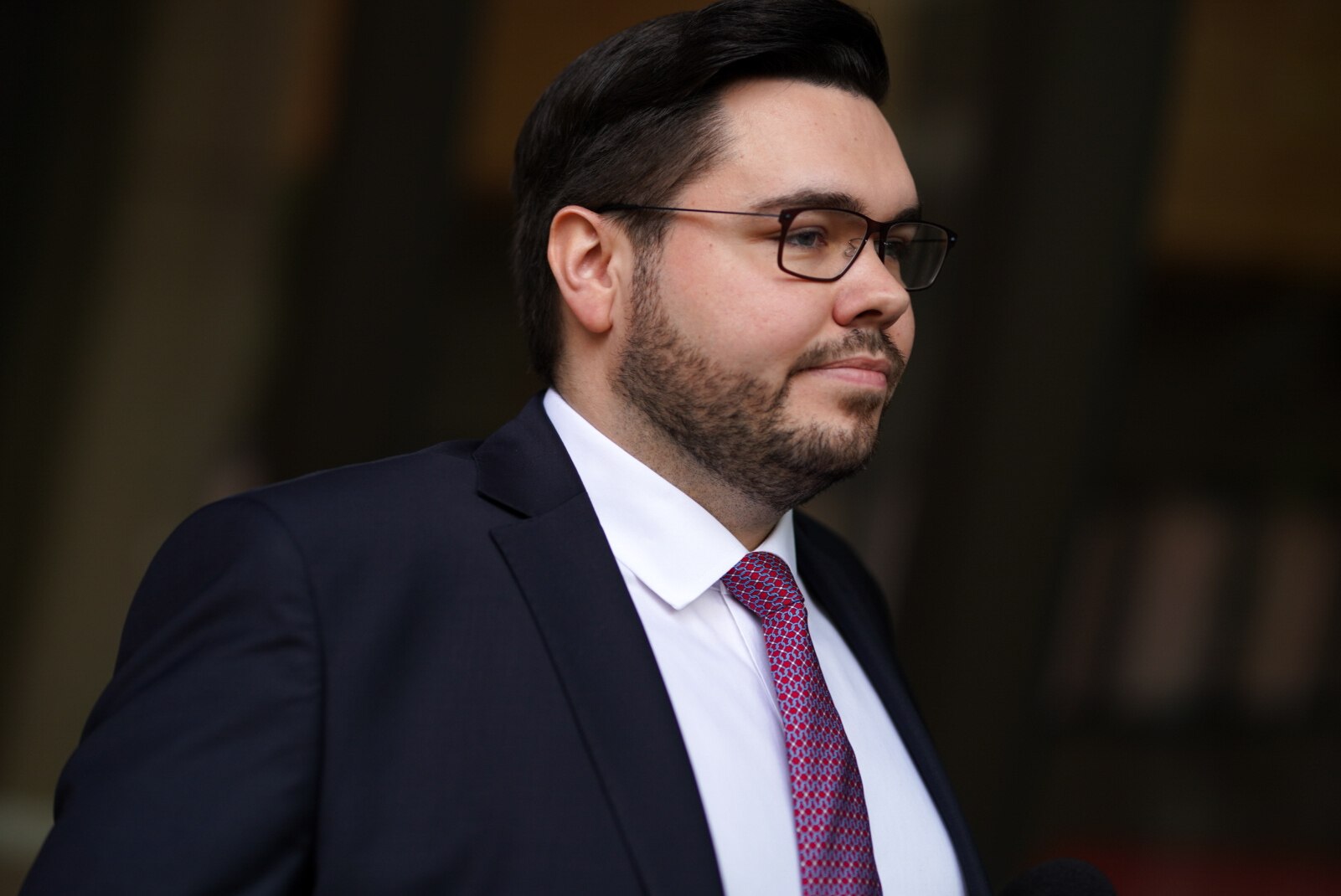 A man wearing a suit and glasses walks down a street.