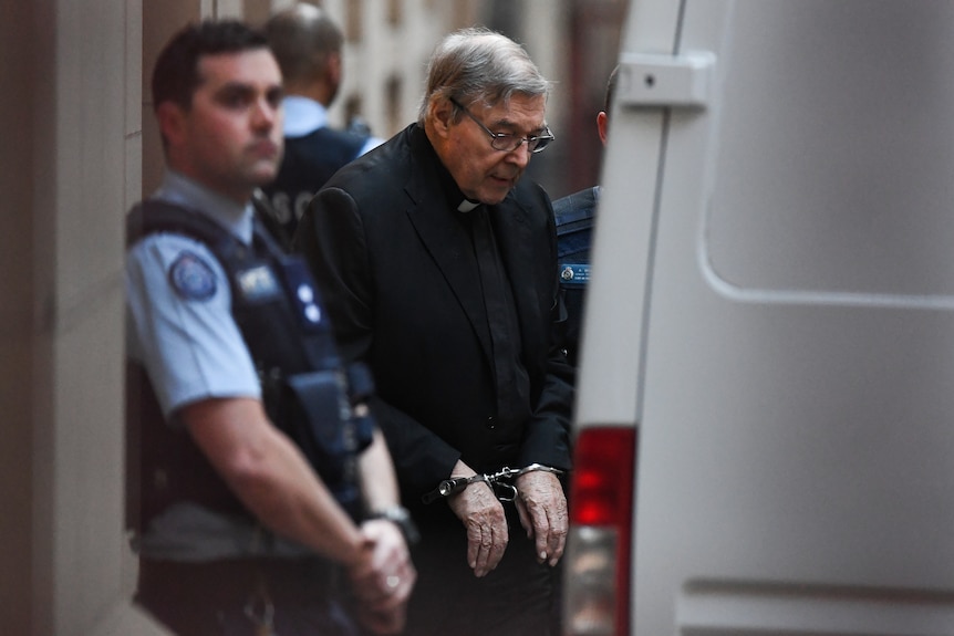 Old man in black religious robe in handcuffs next to police officer