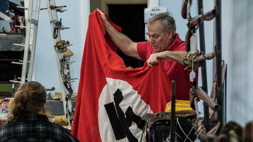 A man holds up a Nazi flag to show a crowd at an auction.