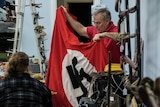 A man holds up a Nazi flag to show a crowd at an auction.