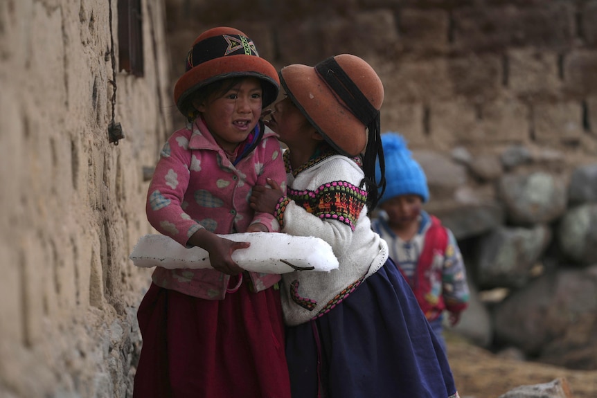 One girl holds a long block of ice as another girl grabs her arm to whisper something in her ear. 